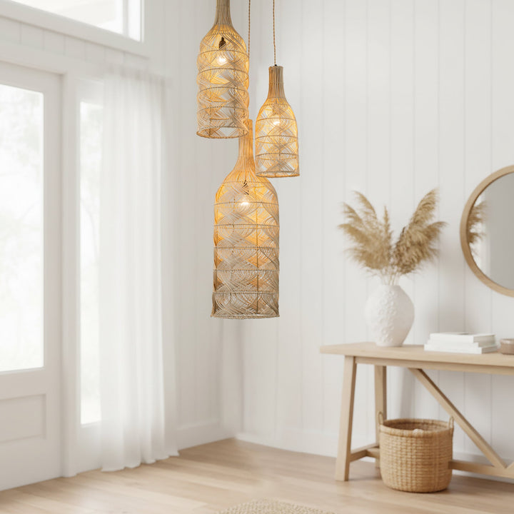 Three woven rattan bottle pendant lights in varying sizes hanging in a bright, modern white room with a wooden console table and pampas grass.